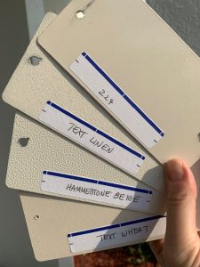 Hand holding paint sample cards in beige shades.