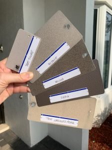 Person holding five paint color samples outdoors.