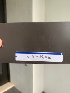 Metal sample labeled 'Super Bronze' held by hand.