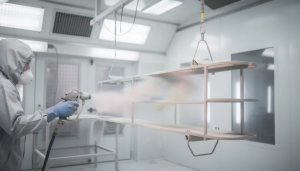 Technician spray painting metal in cleanroom.