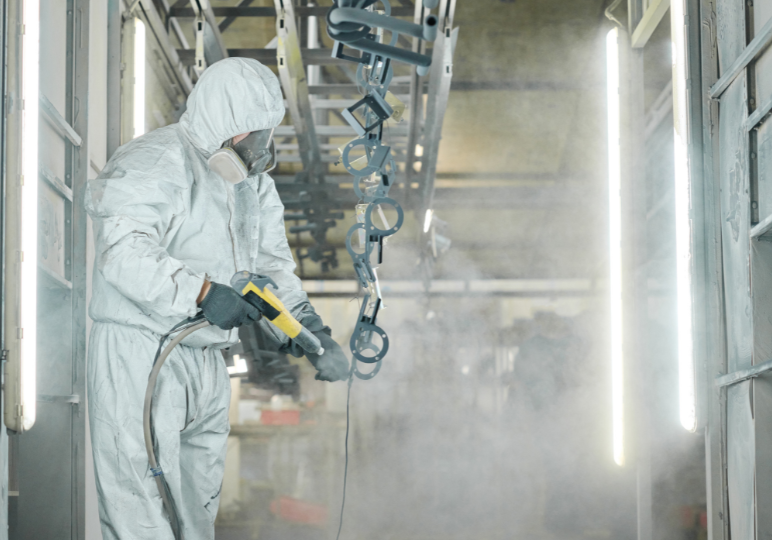 Worker sprays paint in protective gear.