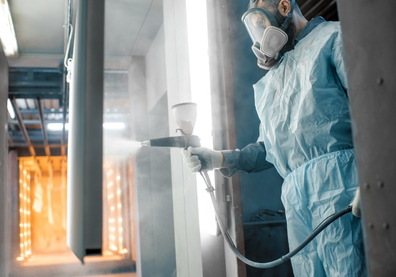 Worker spray painting metal in protective gear