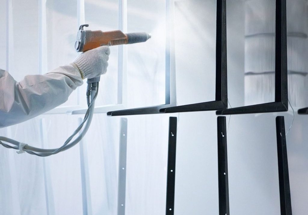 Person spray painting metal frames in booth.
